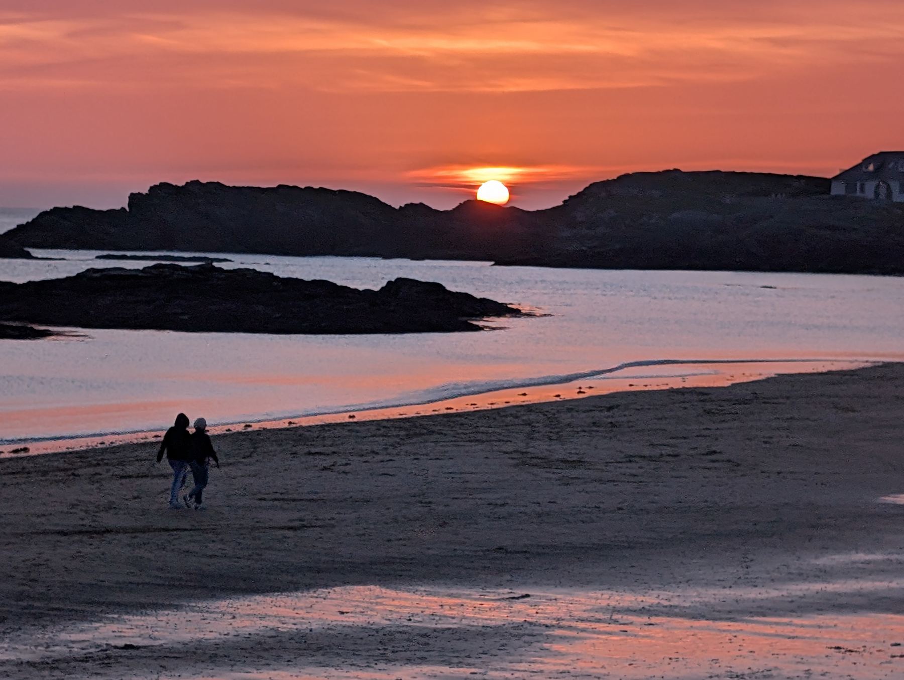 Two people walking together along a beach at sunset