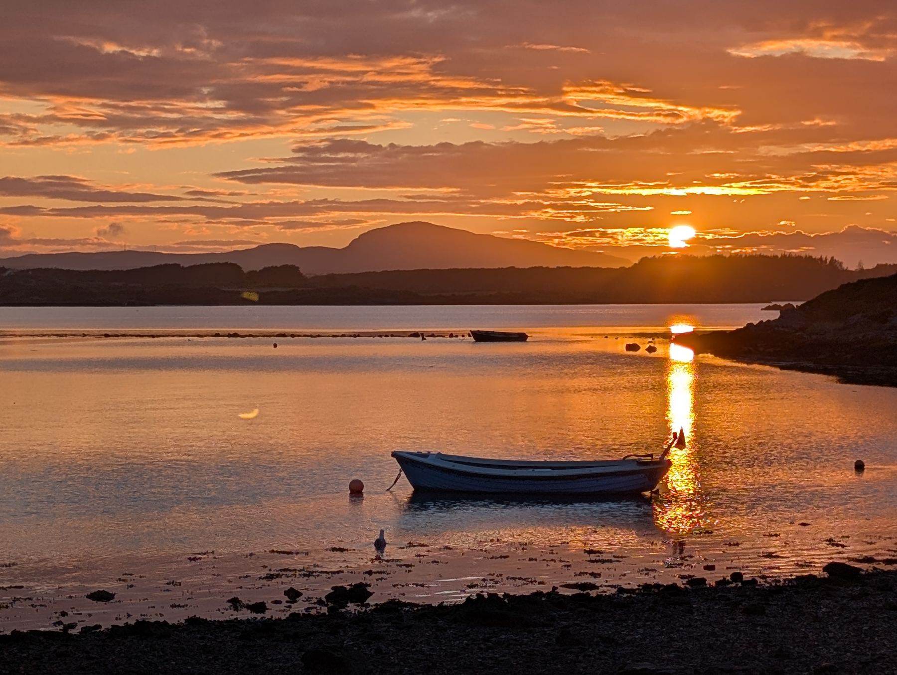 A small boat at anchor in a calm bay at sunset