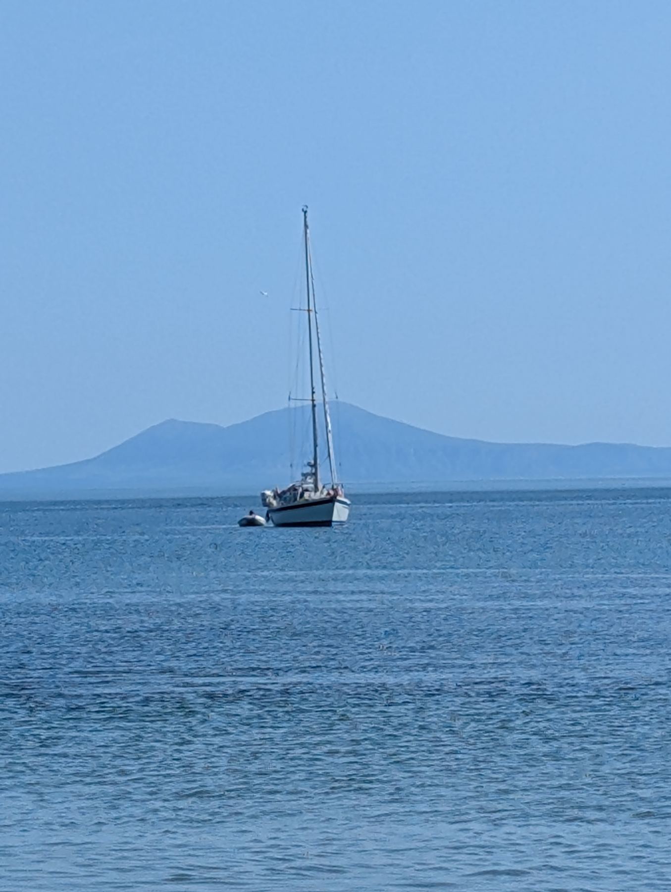 A sailboat at anchor on calm water with Holyhead Mountain beyond